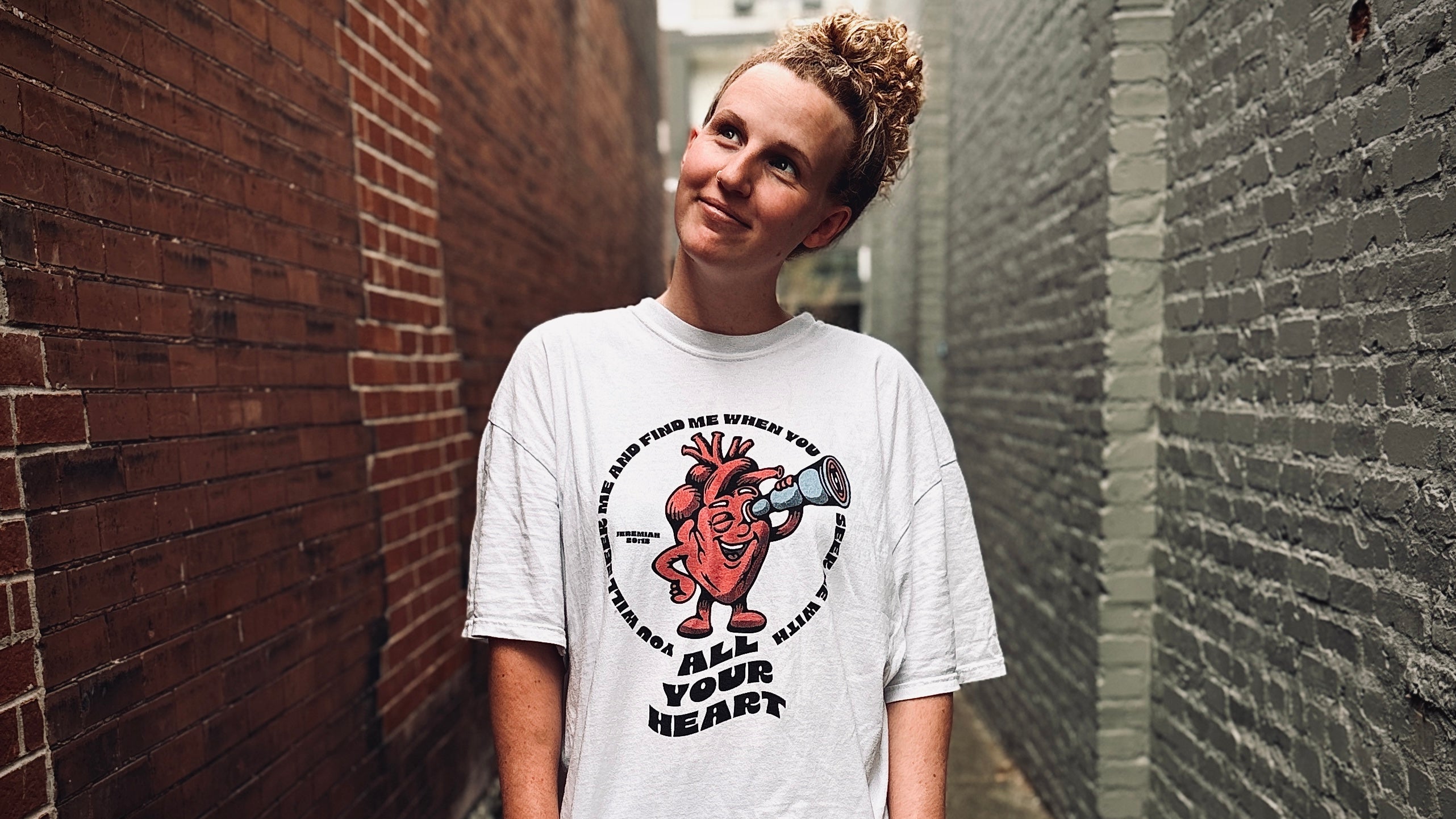 Person wearing a white t-shirt with a graphic design in an alleyway.